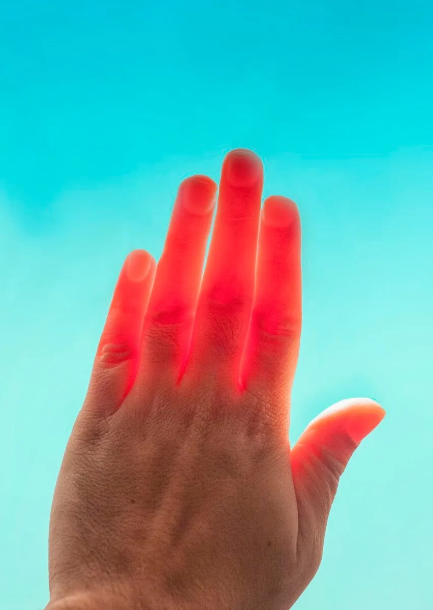 A hand raised against a turquoise sky, its fingers glowing red from behind.