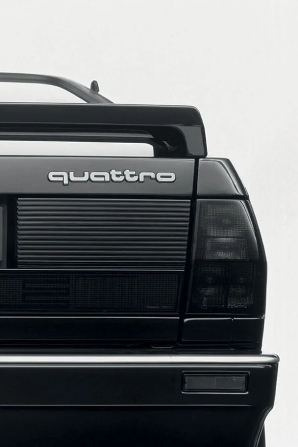The black rear of a car against a white background, with the word quattro on the tailgate and dark tail lights.