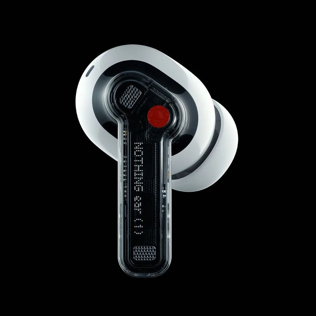 A white wireless earbud with a clear stem on a black ground, showing its inner parts and a red dot, with dot-matrix lettering along the stem.